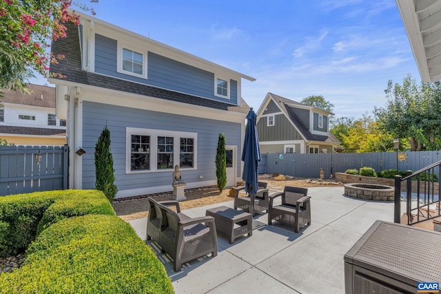 rear view of house with a shingled roof, a fenced backyard, a patio area, and an outdoor living space with a fire pit