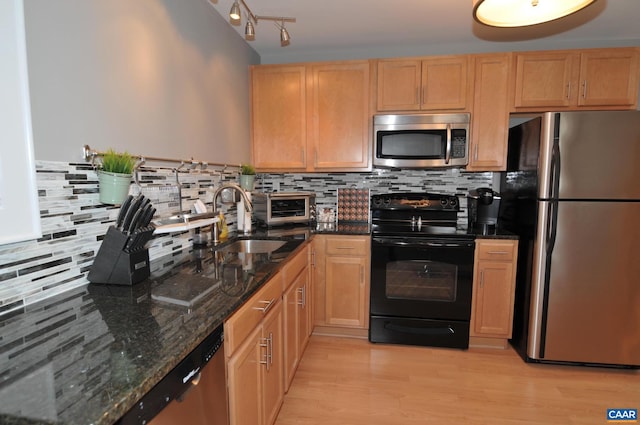 kitchen with appliances with stainless steel finishes, a sink, decorative backsplash, and light wood finished floors