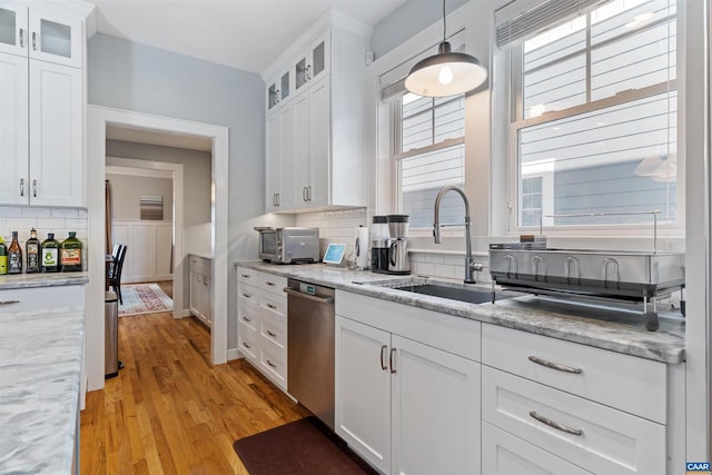 kitchen with decorative backsplash, dishwasher, white cabinets, light wood-style floors, and a sink