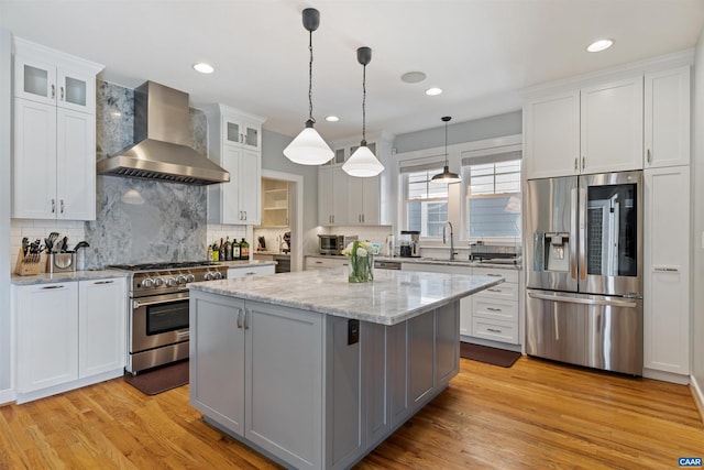 kitchen featuring light wood-type flooring, wall chimney range hood, a kitchen island, and appliances with stainless steel finishes