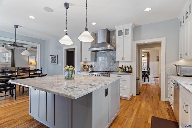 kitchen with stove, a kitchen island, light wood-style floors, wall chimney range hood, and backsplash