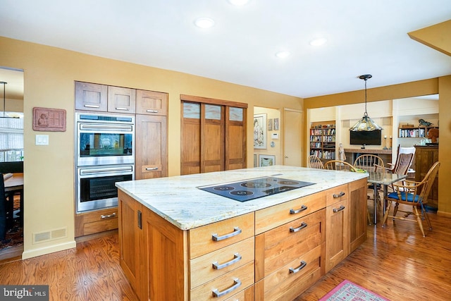 kitchen with black electric stovetop, stainless steel double oven, light wood-style flooring, visible vents, and decorative light fixtures