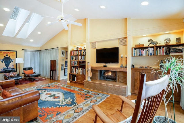 living room with high vaulted ceiling, a skylight, a fireplace, wood finished floors, and visible vents