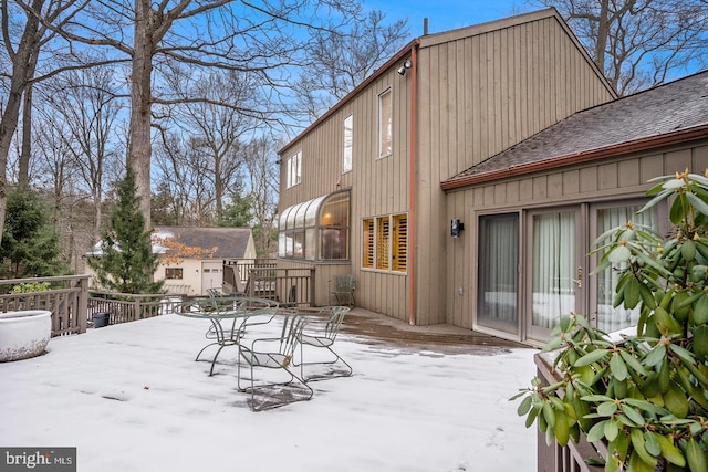 snow covered house with roof with shingles and a wooden deck