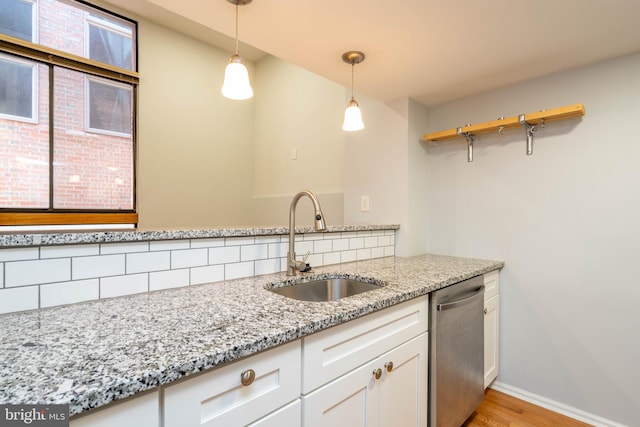 kitchen with light stone counters, decorative light fixtures, white cabinets, a sink, and dishwasher