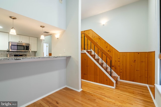 kitchen with decorative light fixtures, stainless steel microwave, light wood-style flooring, decorative backsplash, and white cabinets