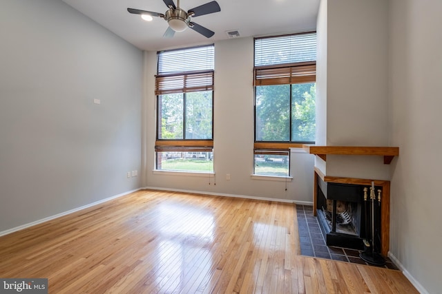 unfurnished living room with wood-type flooring, visible vents, baseboards, and a tiled fireplace