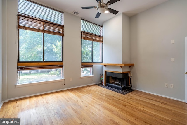 unfurnished living room featuring a multi sided fireplace, a ceiling fan, visible vents, baseboards, and hardwood / wood-style floors