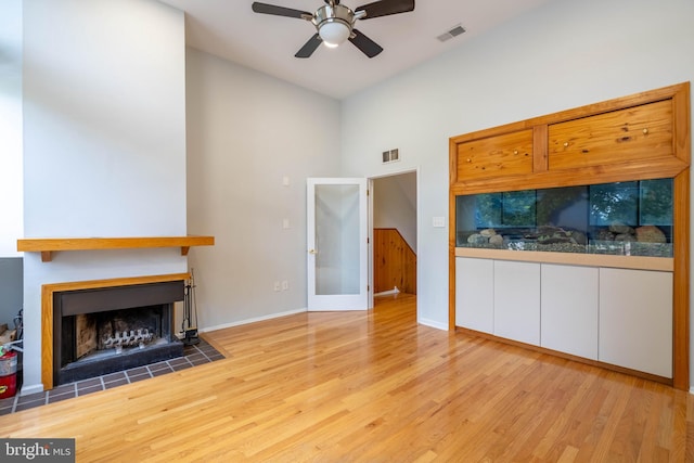 living area with a fireplace with flush hearth, wood finished floors, visible vents, and a ceiling fan