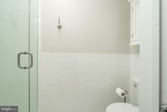 full bathroom with an enclosed shower, toilet, and tile walls