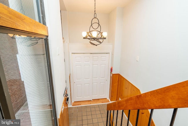 doorway to outside featuring a wainscoted wall, wooden walls, tile patterned flooring, and a notable chandelier