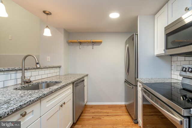 kitchen with light wood finished floors, tasteful backsplash, stainless steel appliances, white cabinetry, and a sink