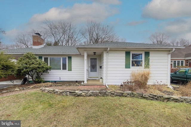 single story home with a chimney, a front lawn, and roof with shingles