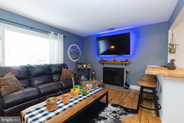 living area with a fireplace with flush hearth, visible vents, light wood-style floors, and baseboards