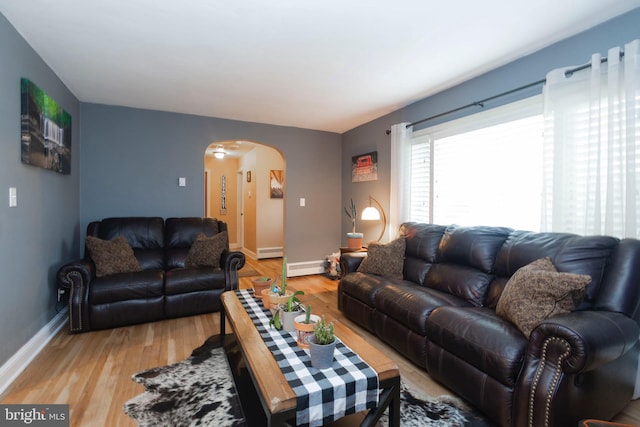 living room featuring light wood-type flooring, arched walkways, baseboards, and a baseboard radiator