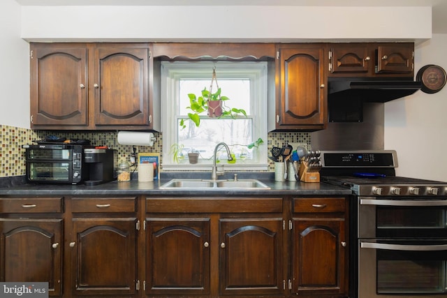 kitchen featuring dark countertops, double oven range, decorative backsplash, and a sink