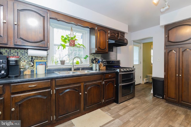 kitchen with decorative backsplash, range with two ovens, dark countertops, light wood-style floors, and a sink