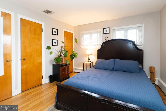 bedroom with baseboard heating, baseboards, visible vents, and light wood finished floors