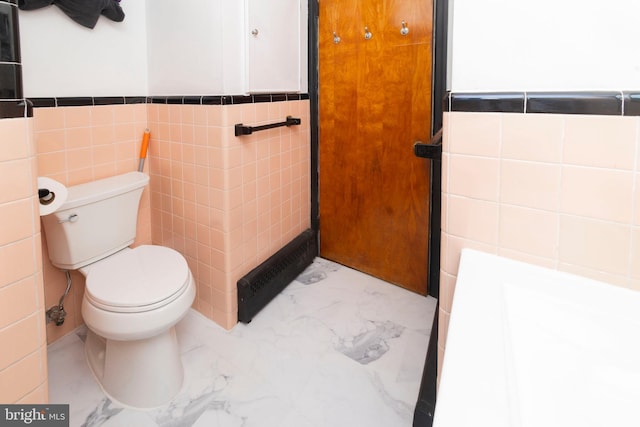 bathroom with marble finish floor, wainscoting, tile walls, and toilet