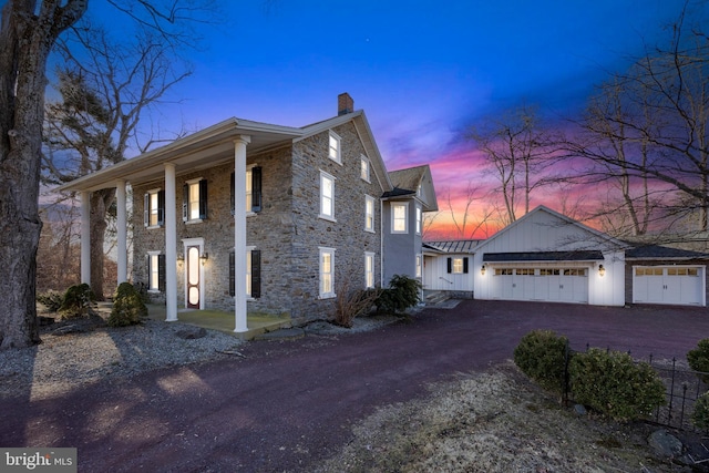 exterior space with metal roof, aphalt driveway, an attached garage, a standing seam roof, and a chimney