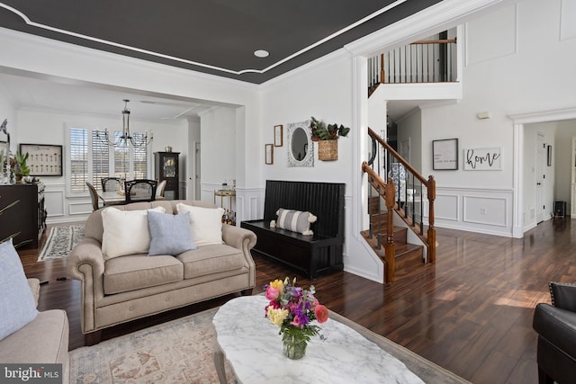 living area with stairs, a decorative wall, wood finished floors, and ornamental molding