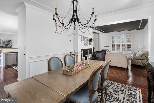 dining space with a wainscoted wall, wood finished floors, an inviting chandelier, and ornamental molding