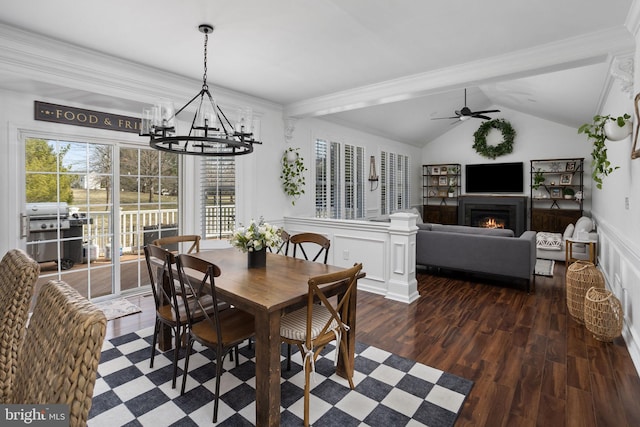 dining space featuring lofted ceiling, ornamental molding, ceiling fan with notable chandelier, a warm lit fireplace, and wood finished floors