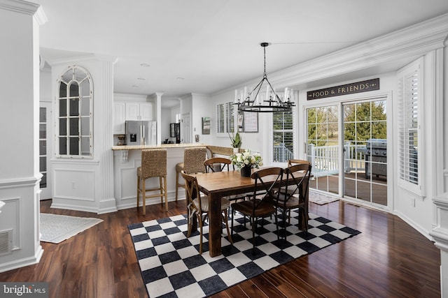 dining area featuring decorative columns, dark wood-type flooring, crown molding, and a notable chandelier