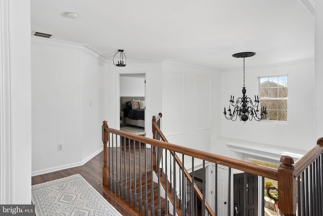 corridor featuring visible vents, an upstairs landing, ornamental molding, dark wood finished floors, and a chandelier