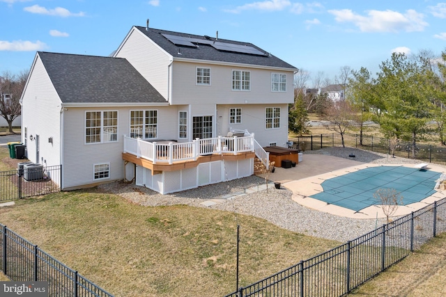 rear view of property with roof mounted solar panels, a lawn, a wooden deck, and a fenced backyard