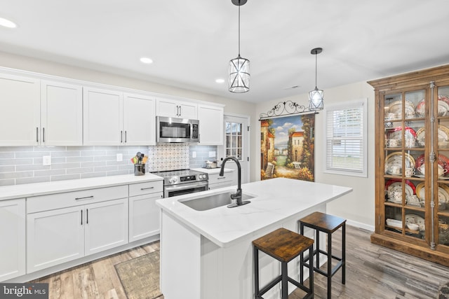 kitchen with light wood finished floors, white cabinets, decorative backsplash, appliances with stainless steel finishes, and a sink