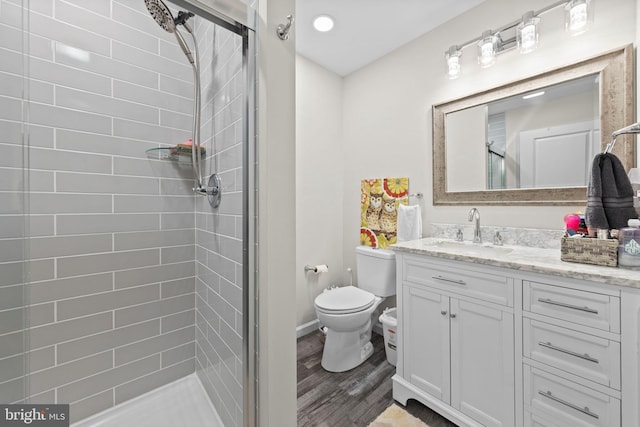 full bath with toilet, a shower stall, vanity, wood finished floors, and baseboards