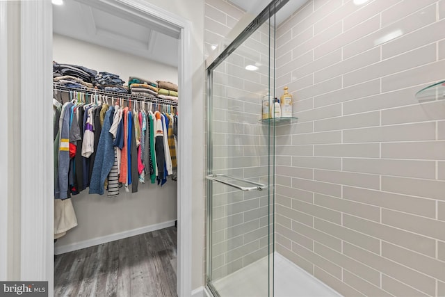 full bathroom with a shower stall, a spacious closet, baseboards, and wood finished floors