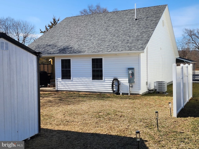 rear view of property featuring roof with shingles, fence, a lawn, and central air condition unit