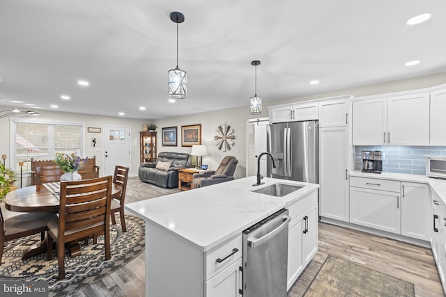 kitchen with stainless steel appliances, a sink, light wood-type flooring, tasteful backsplash, and a center island with sink