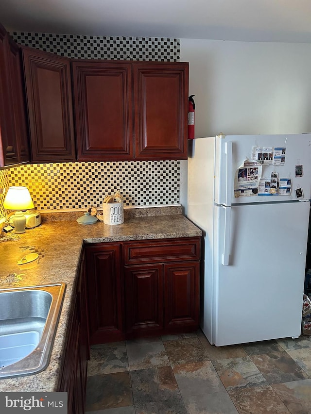 kitchen with stone finish flooring, decorative backsplash, a sink, and freestanding refrigerator