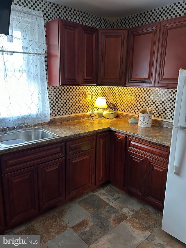 kitchen with tasteful backsplash, stone finish floor, a sink, and freestanding refrigerator