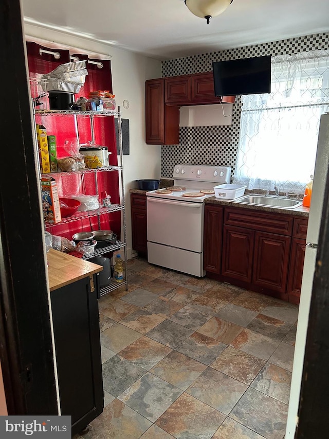 kitchen with electric stove, tasteful backsplash, freestanding refrigerator, stone finish flooring, and a sink