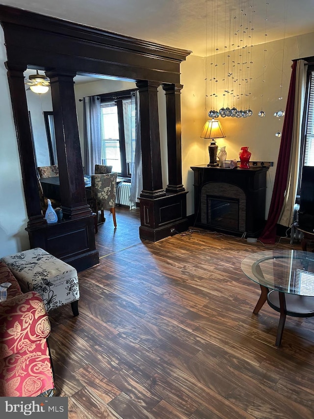 sitting room with radiator heating unit, a fireplace, wood finished floors, and decorative columns