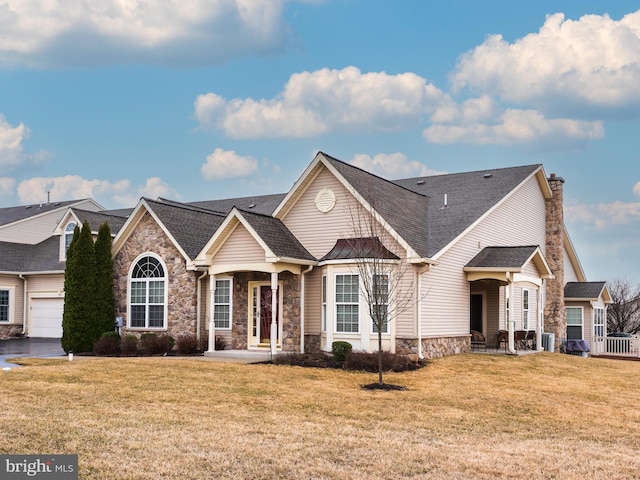 view of front of house with stone siding, a shingled roof, a chimney, and a front lawn