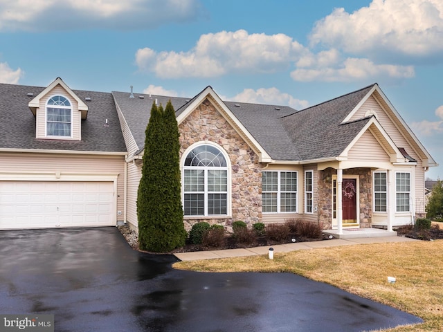 view of front of house with driveway, a front lawn, roof with shingles, and stone siding