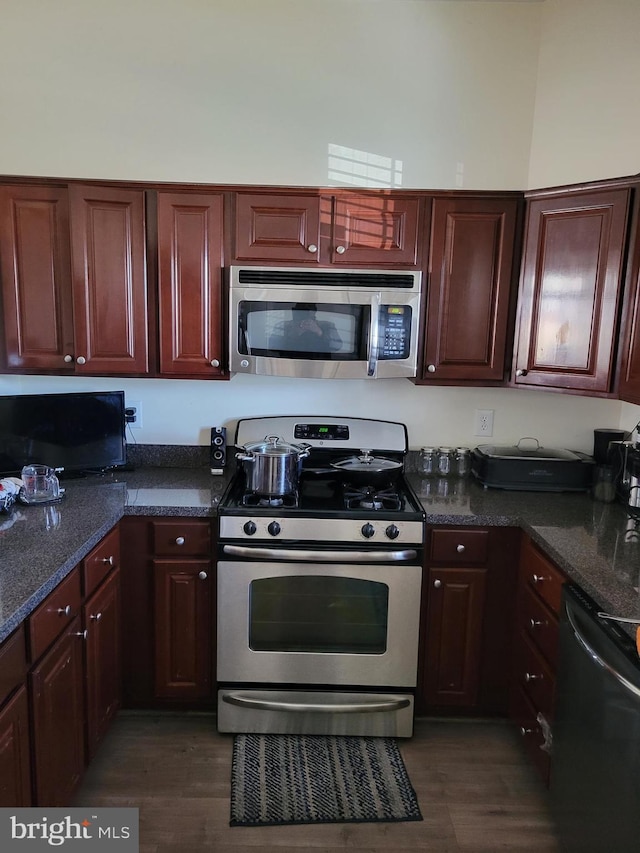 kitchen with appliances with stainless steel finishes, dark stone counters, dark wood-type flooring, and dark brown cabinets