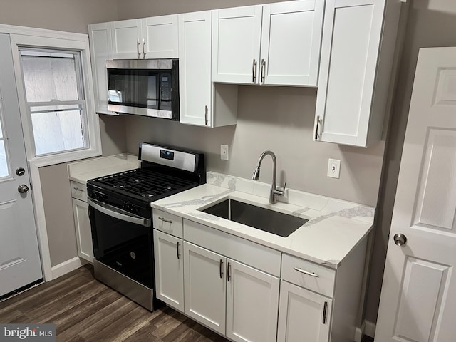 kitchen featuring light stone counters, stainless steel appliances, a sink, white cabinets, and dark wood finished floors