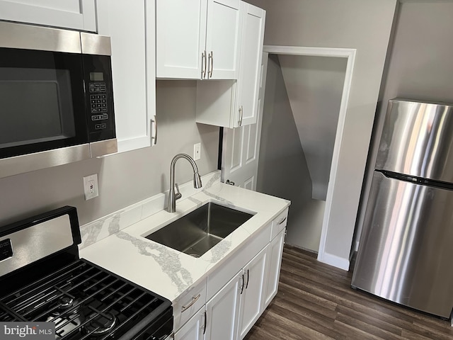 kitchen with appliances with stainless steel finishes, dark wood-type flooring, white cabinets, a sink, and light stone countertops