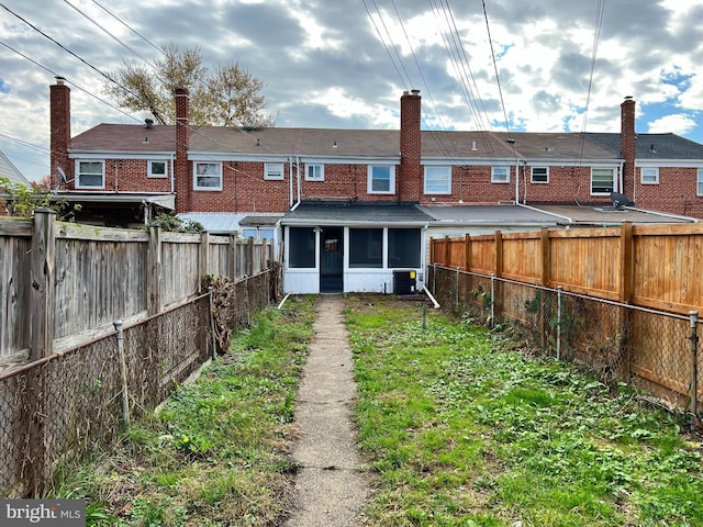 rear view of house with cooling unit, a sunroom, a fenced backyard, and brick siding