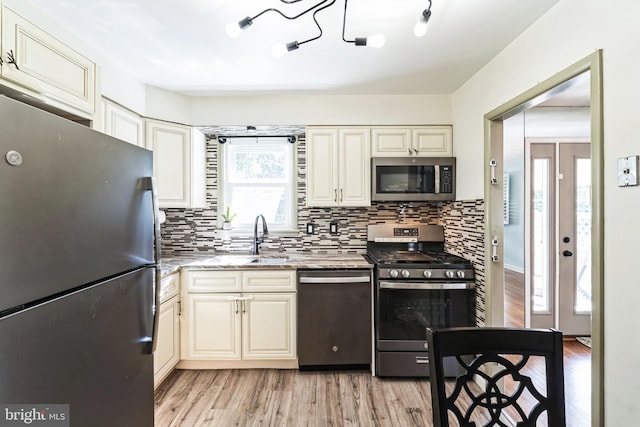 kitchen featuring light wood-style flooring, appliances with stainless steel finishes, a sink, light stone countertops, and backsplash