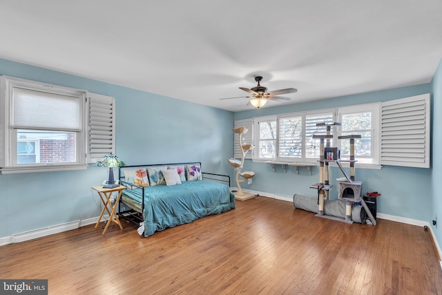 bedroom with a ceiling fan, baseboards, baseboard heating, wood-type flooring, and a wood stove