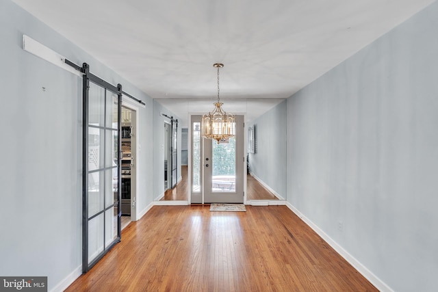 doorway to outside featuring a barn door, baseboards, a chandelier, and wood finished floors