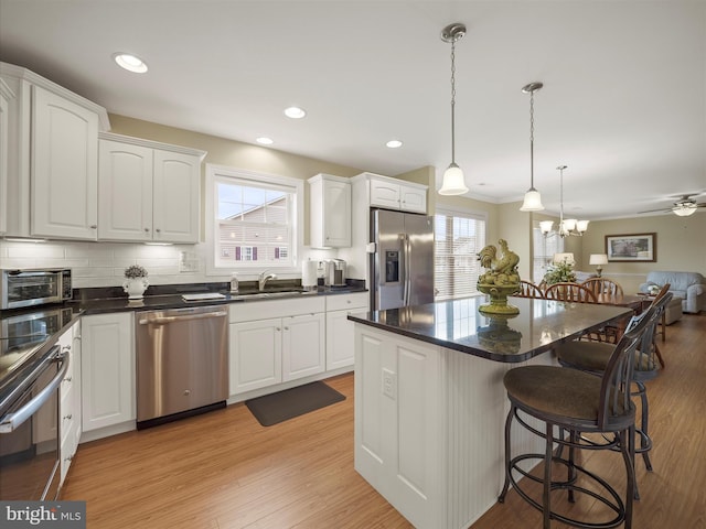 kitchen with light wood-style flooring, a breakfast bar area, stainless steel appliances, white cabinetry, and a sink