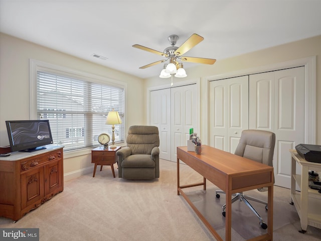 office space featuring a ceiling fan, light colored carpet, visible vents, and baseboards